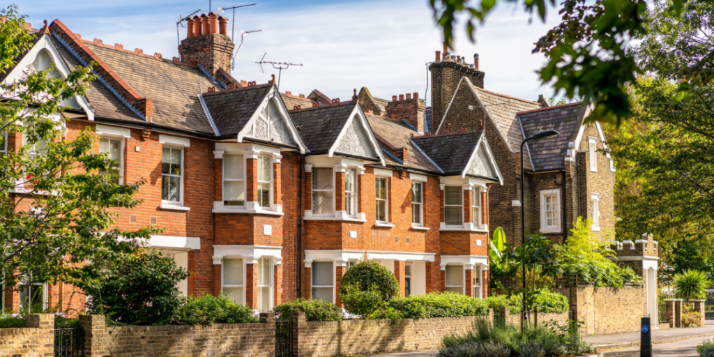 Row of traditional red-brick Victorian terraced houses with bay windows, pitched roofs, and chimneys, set along a leafy residential street in the UK.