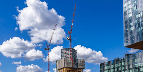Construction cranes and buildings against cloudy blue sky