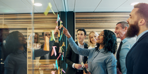 Team of five placing postit notes on a glass wall during meeting