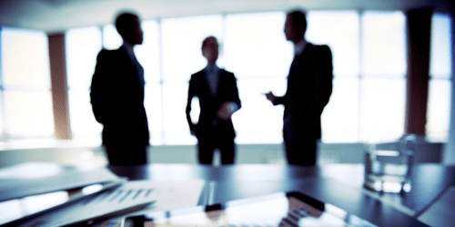 Blurred image of men in suits talking silhouetted against window