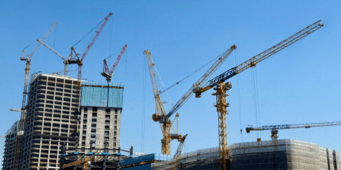 Red and yellow cranes against blue sky background with skyscrapers