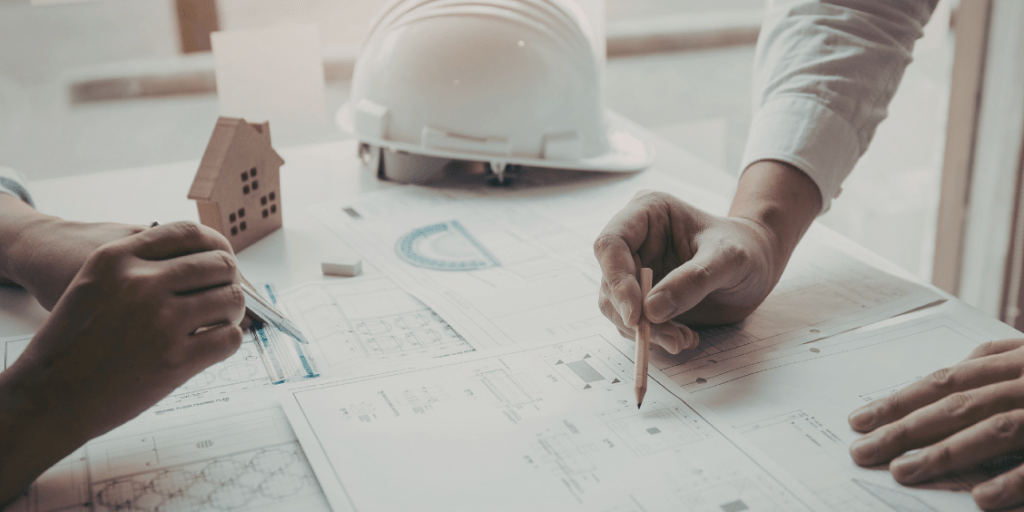 Architects reviewing housing plans and technical drawings spread across a desk.
