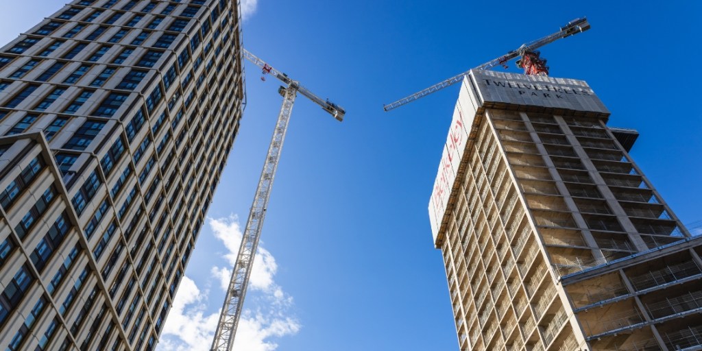 Two tall buildings under construction against a blue sky with cranes nearby