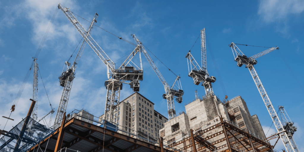 Several tower cranes operating on a construction site beneath a blue sky.