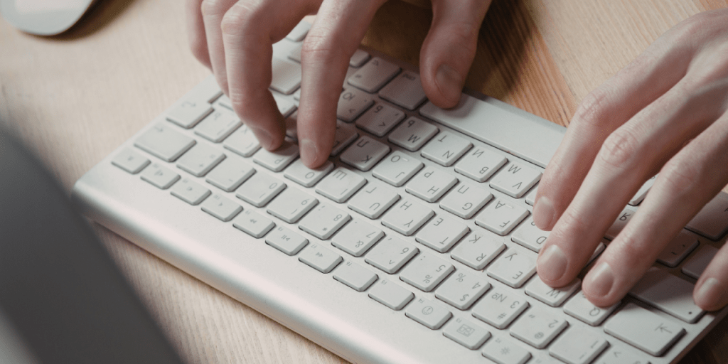 Hands typing on a white keyboard at a desk