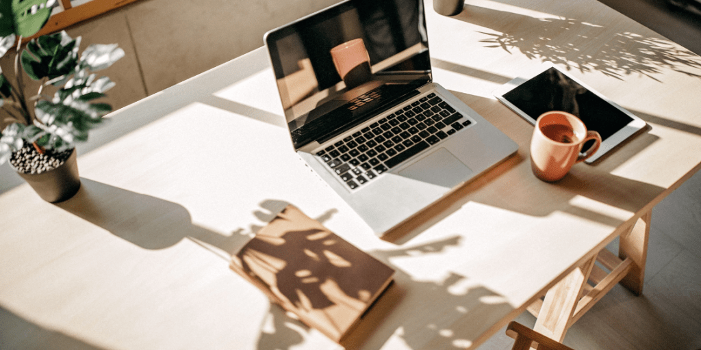 Laptop on a desk with a coffee cup, tablet and plant