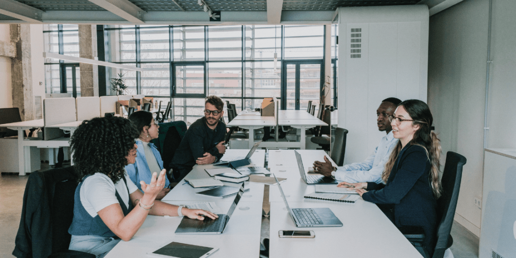 Colleagues collaborating around a table in an open-plan office with laptops