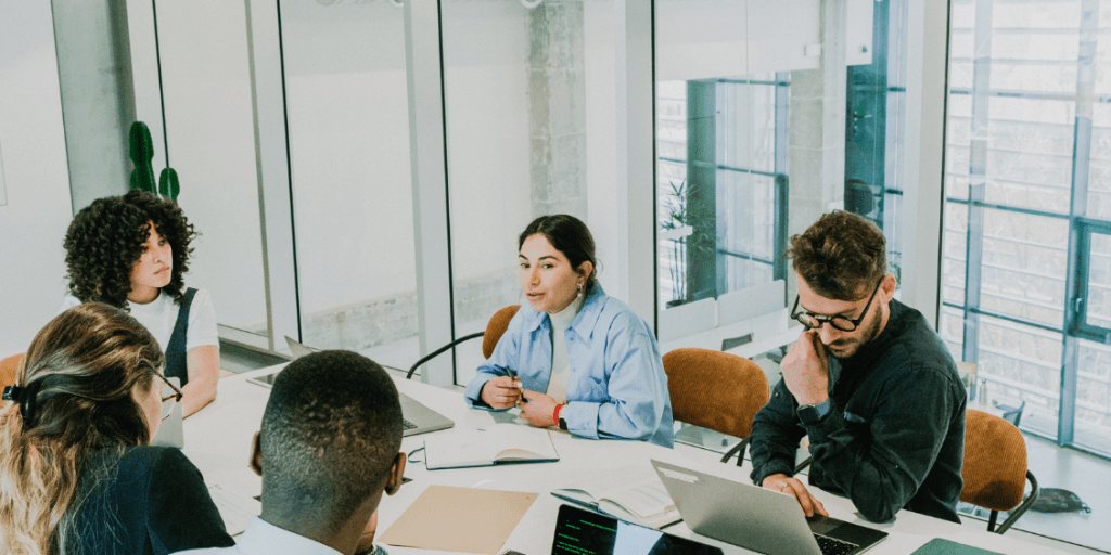 People discussing and working on laptops in a glass-walled boardroom