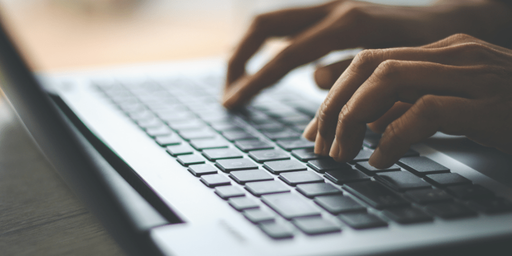 Close-up of hands typing on a laptop keyboard on a shaded desk.