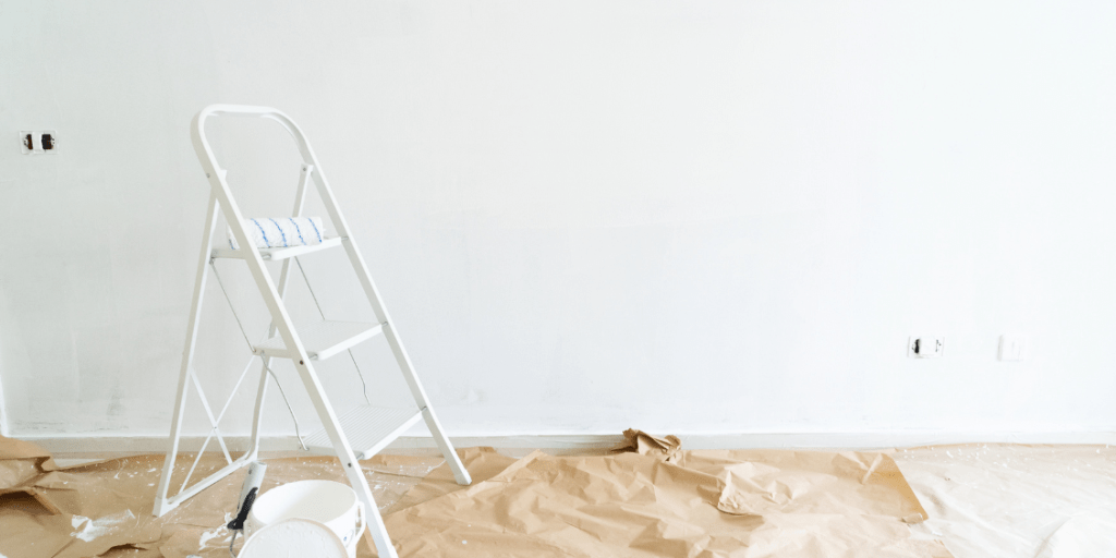 Ladder beside a white wall with paint and protective floor covering.