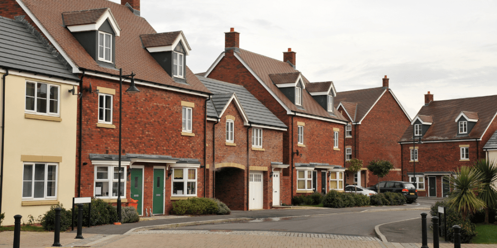 New-build residential street with terraced homes, parked cars, and street lamps.