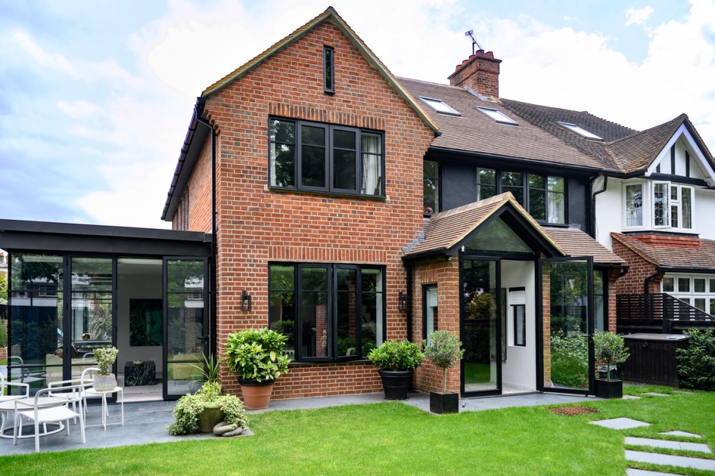 Back yard view of modern two-storey home in early summer with green grass, potted plants, patio table and chairs.