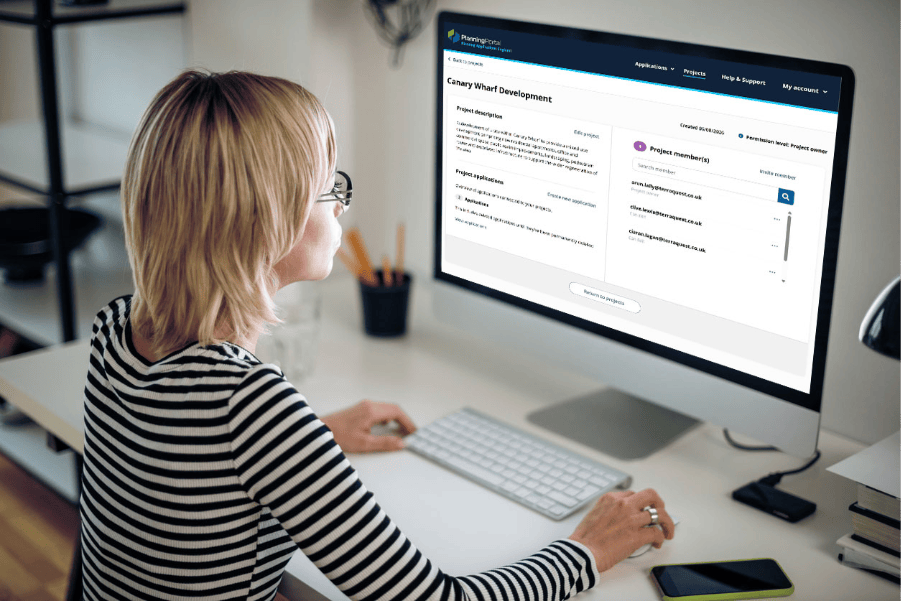 A woman working at a desktop computer displaying the Planning Portal multiple projects platform.