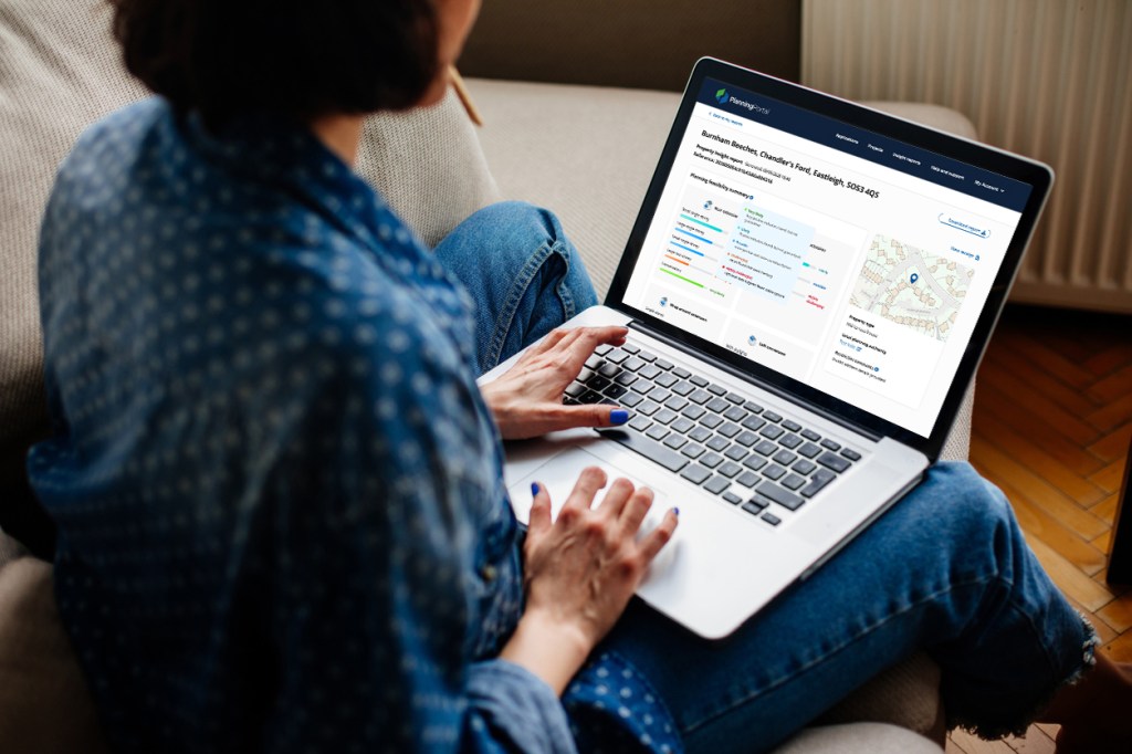 A person sitting on a couch using a laptop, displaying a webpage with property information and a map.