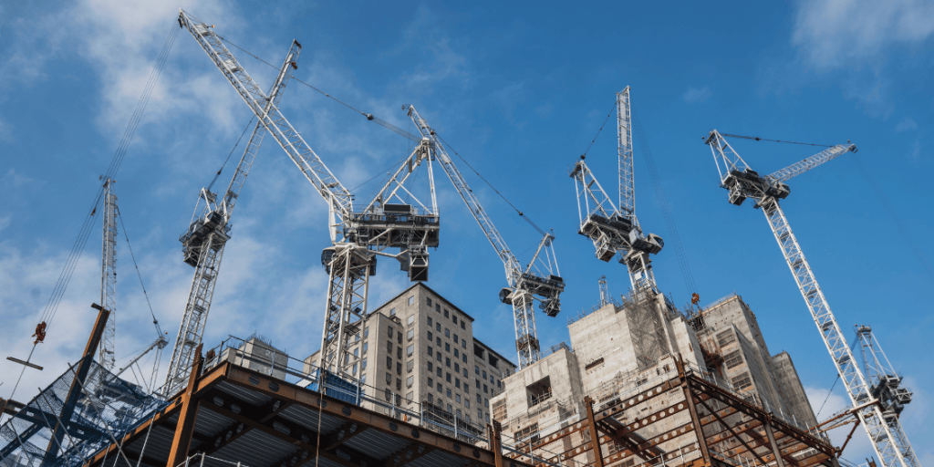 Construction site with multiple cranes and a partially completed building against a blue sky.